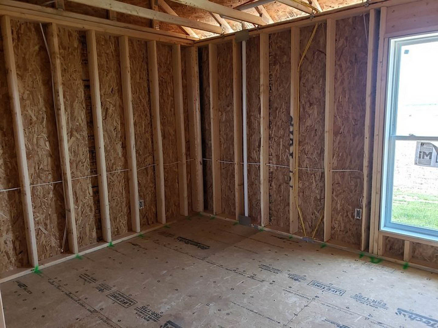 Wood-beamed ceiling and plank floor in a room with a window and door, newspaper resting on the window sill, white walls, natural light illuminating interior.