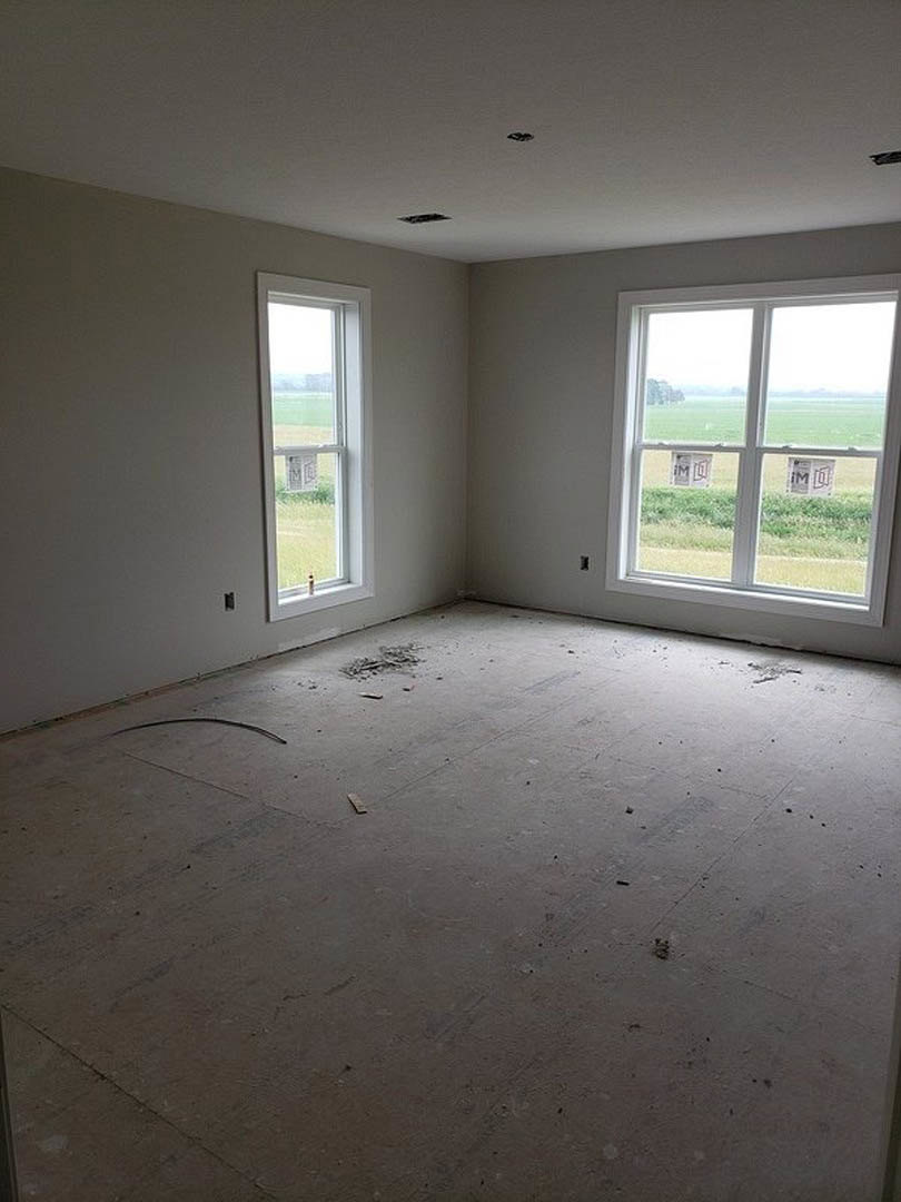 Spacious room featuring multiple windows, polished concrete floor, white plaster walls, circular floor detail, and views of a green field outside
