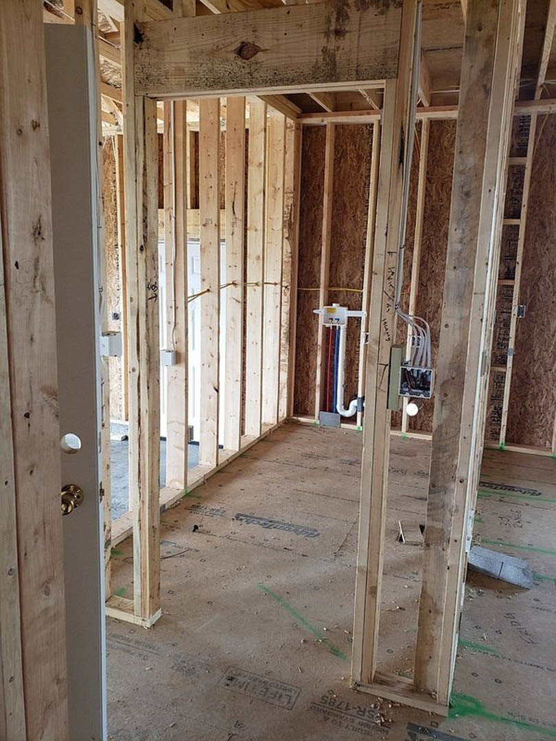 Exposed wood framing with vertical beams, unfinished walls, white door, and visible construction materials in a residential interior.