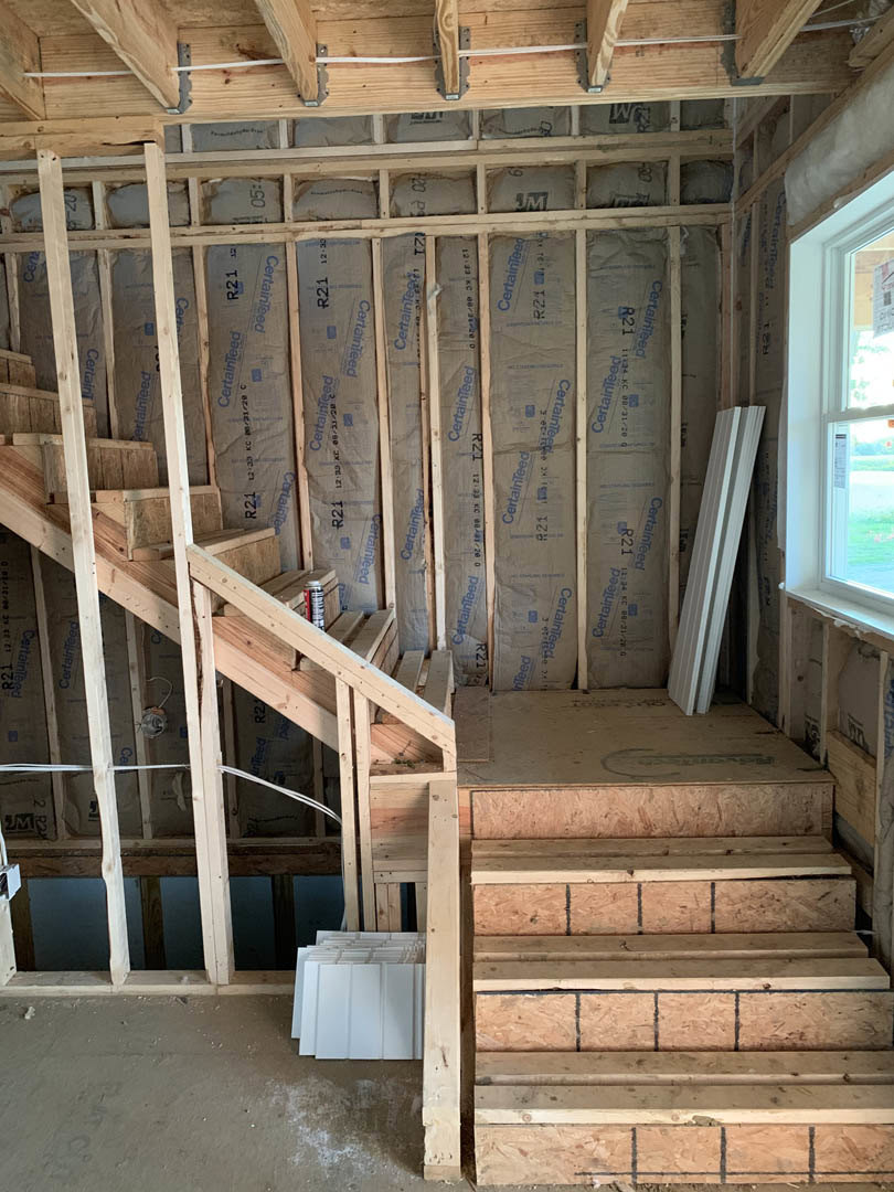 Wooden staircase with white panels and metal beam in unfinished room, exposed lumber, window, and visible electrical cable attached to wood beam