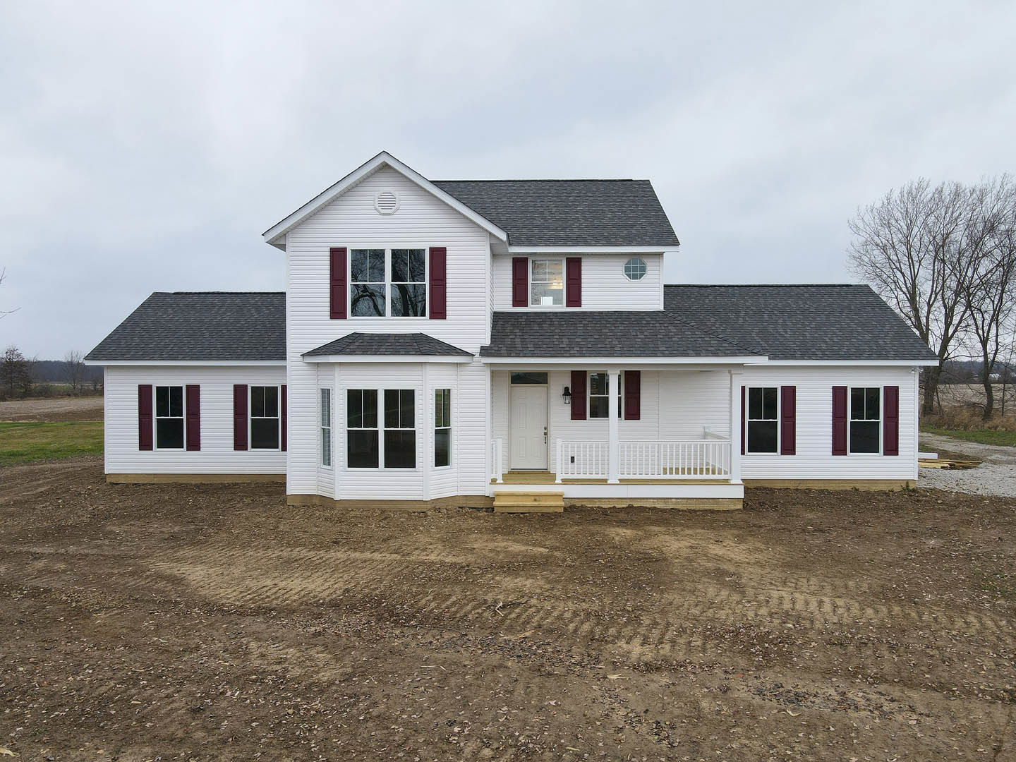 White siding house with red shutters, white front door, metal doorknob, white porch railing, tree and cloudy sky in background