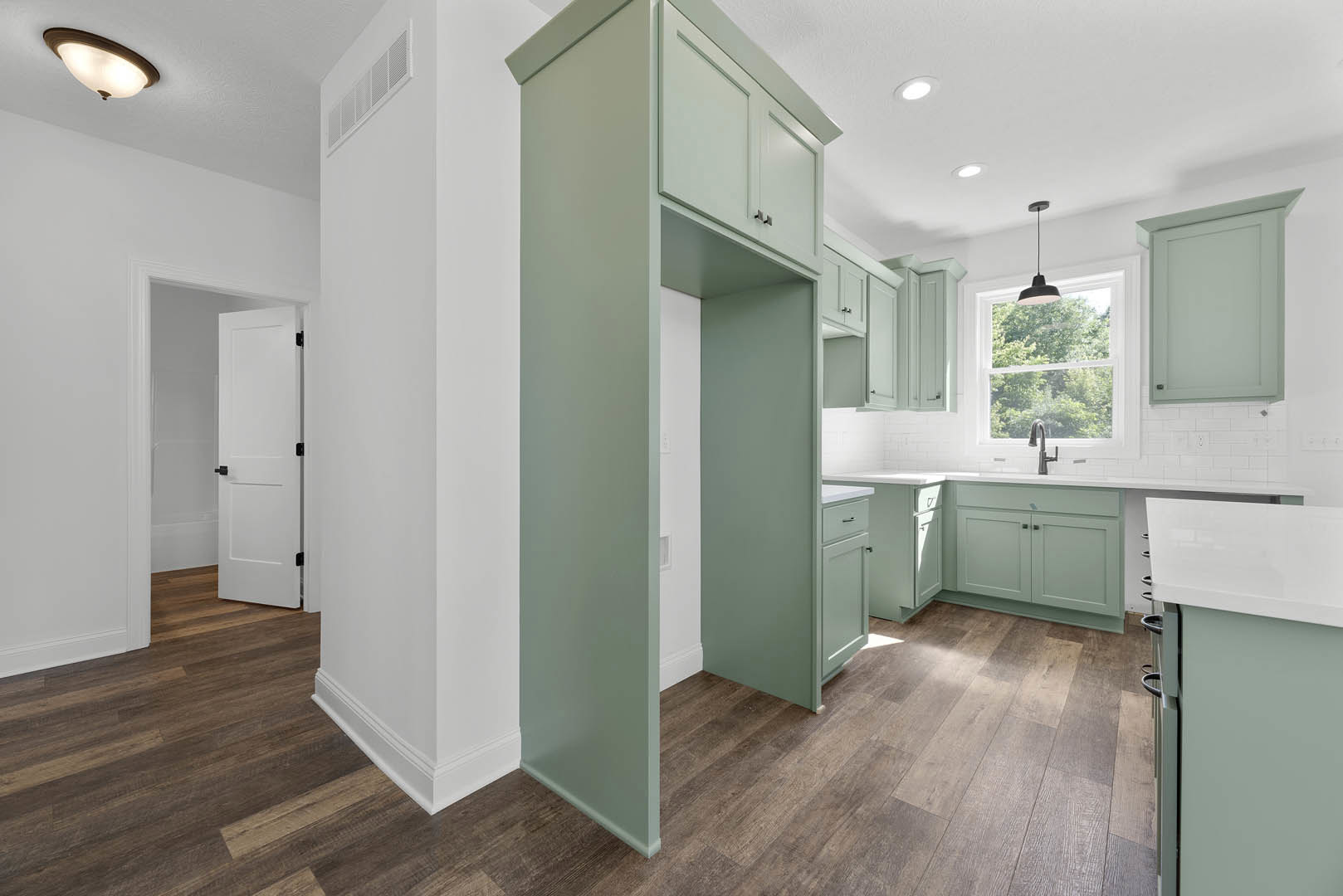Kitchen with wood flooring, white cabinetry, black hardware, ceiling light fixture, white door with white frame, window with overhead light, black object on countertop