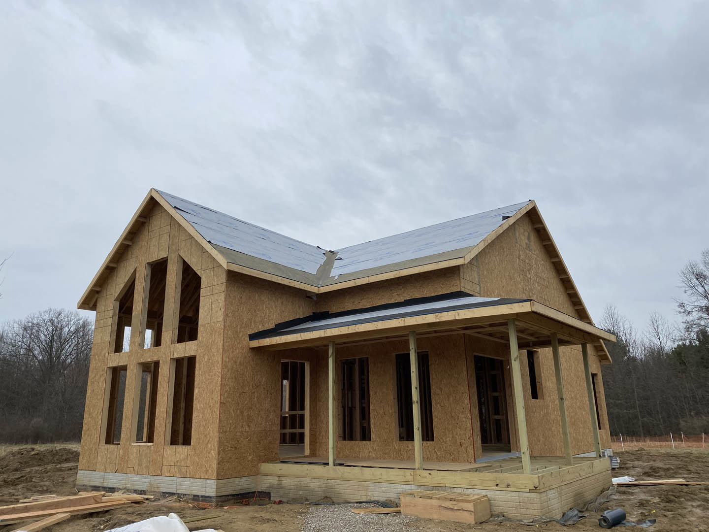 Partially built wooden house with exposed framing, unfinished roof, and large window openings beneath a cloudy sky