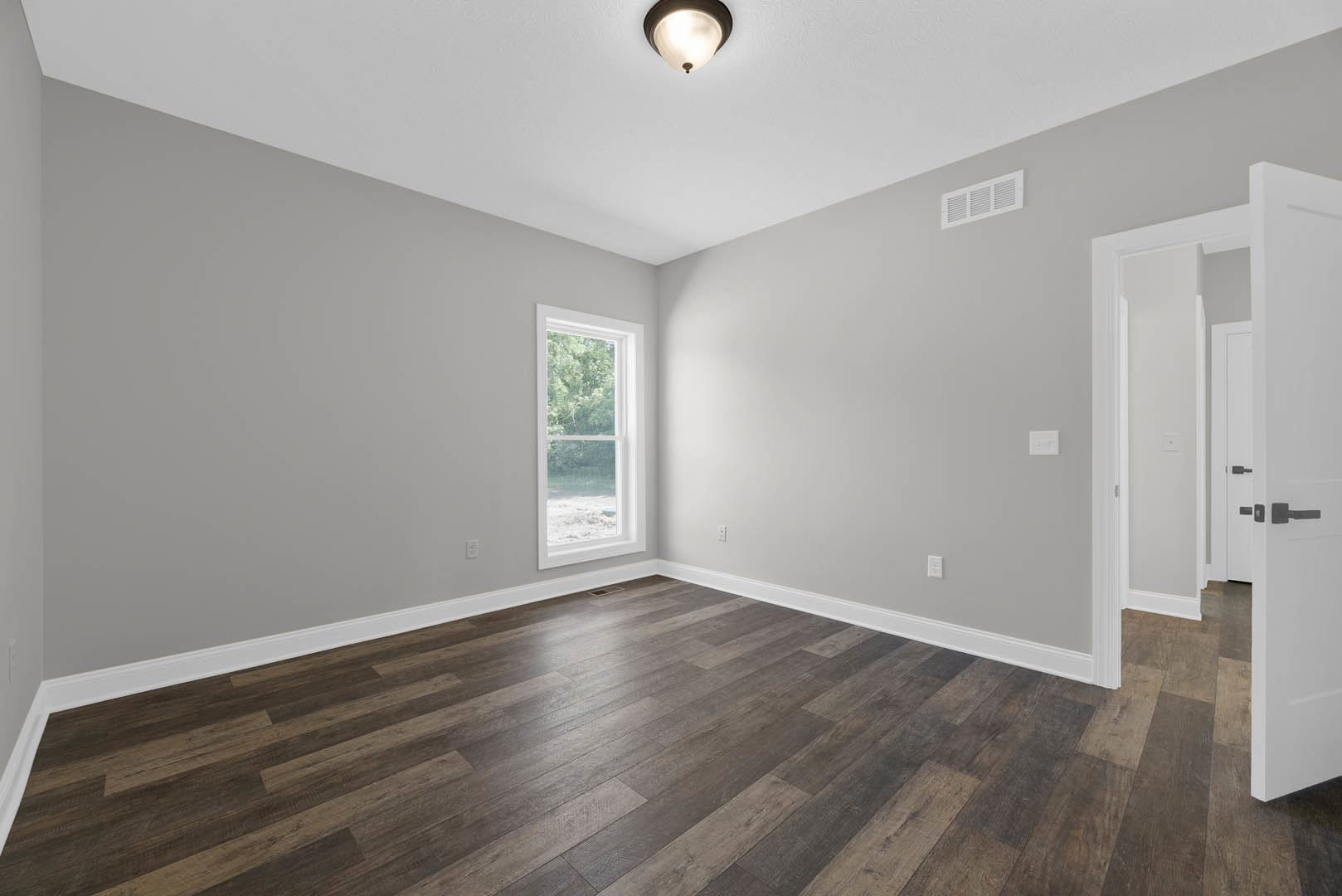 Wood flooring in a bright room with a large white-framed window, ceiling vent, and modern light fixture