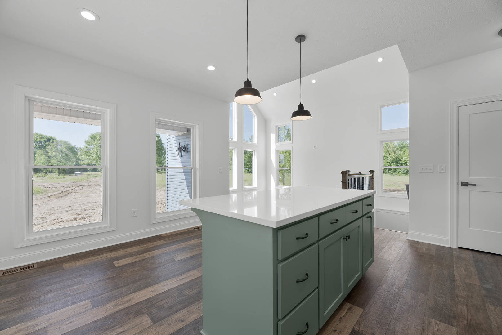 White kitchen island with drawers and smooth countertop, wood plank flooring, ceiling light fixture, window overlooking dirt field, cabinetry and sink along wall