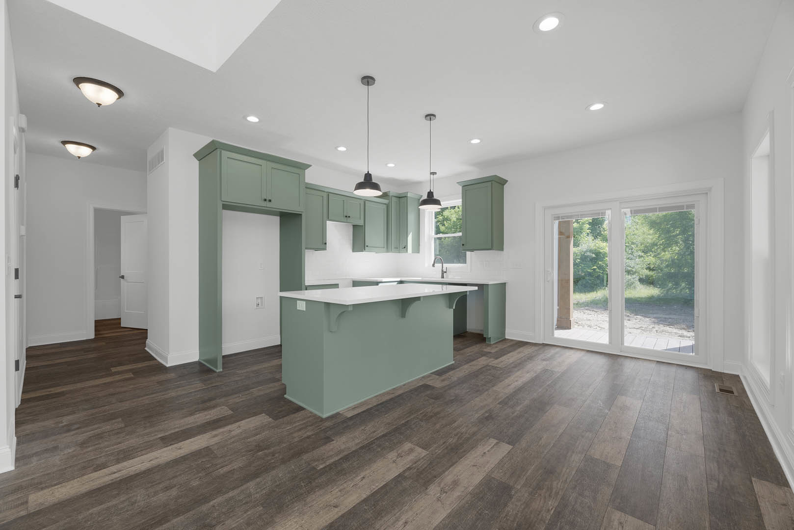 Kitchen with white countertop bar, wood flooring, green accent wall, sliding glass door, modern cabinetry, and recessed lighting.