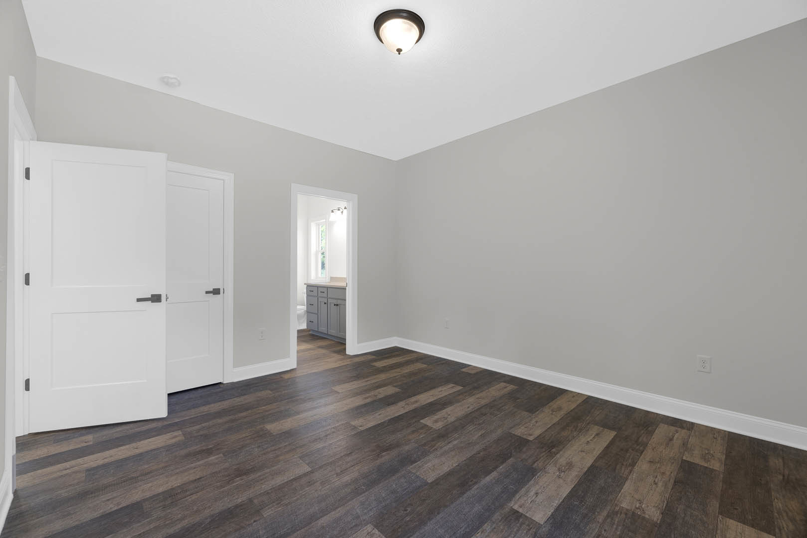 White walls and ceiling, wood plank flooring, white doors with black handles, white cabinet with drawers, window letting in natural light, modern ceiling light fixture