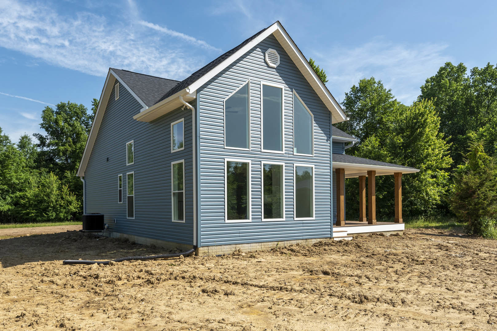 Blue siding house with multiple windows, dirt yard in foreground, green tree visible through window, cloudy sky overhead
