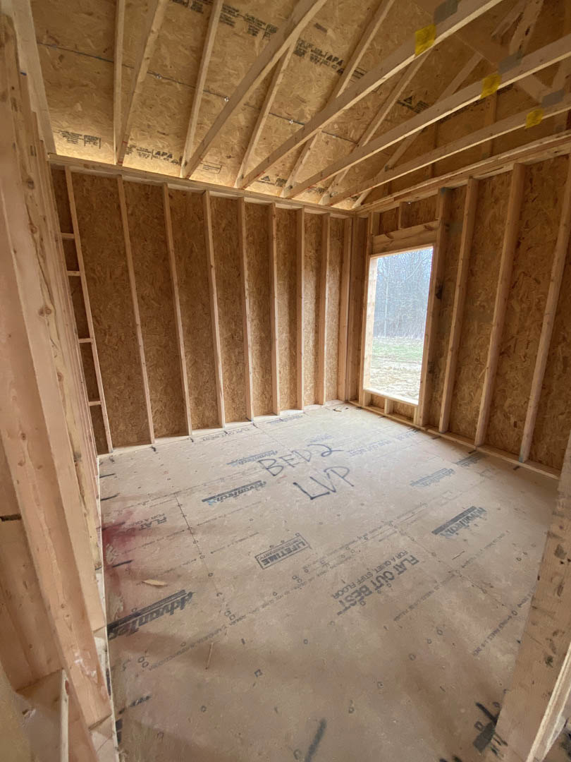 Exposed wood ceiling beams, beige walls, large window with outdoor view, unfinished construction materials visible