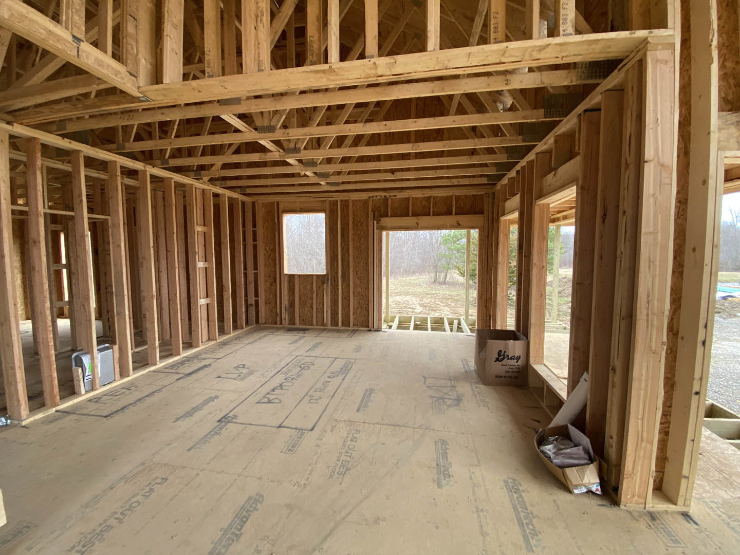 Open living space with wide plank wood flooring, exposed wood ceiling beams, large windows, and neutral walls