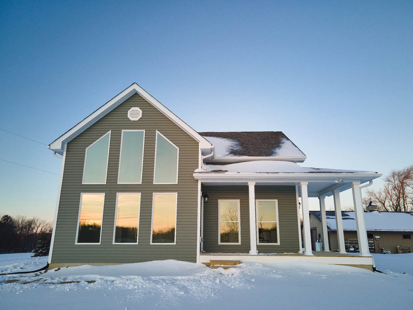 Two-story home with white siding, snow-covered roof and ground, white-trimmed windows, leafless tree outside, and exterior wall vent