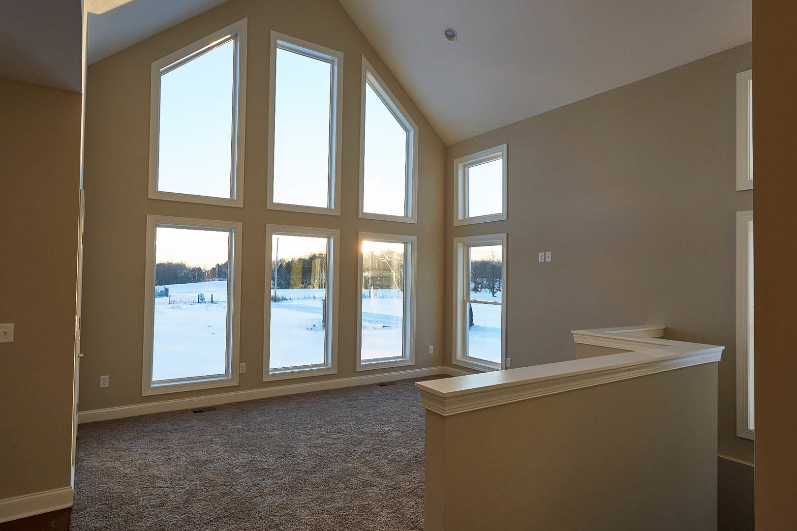 Spacious room featuring multiple large windows, white walls, neutral carpet flooring, and views of clear sky and snowy landscape outside