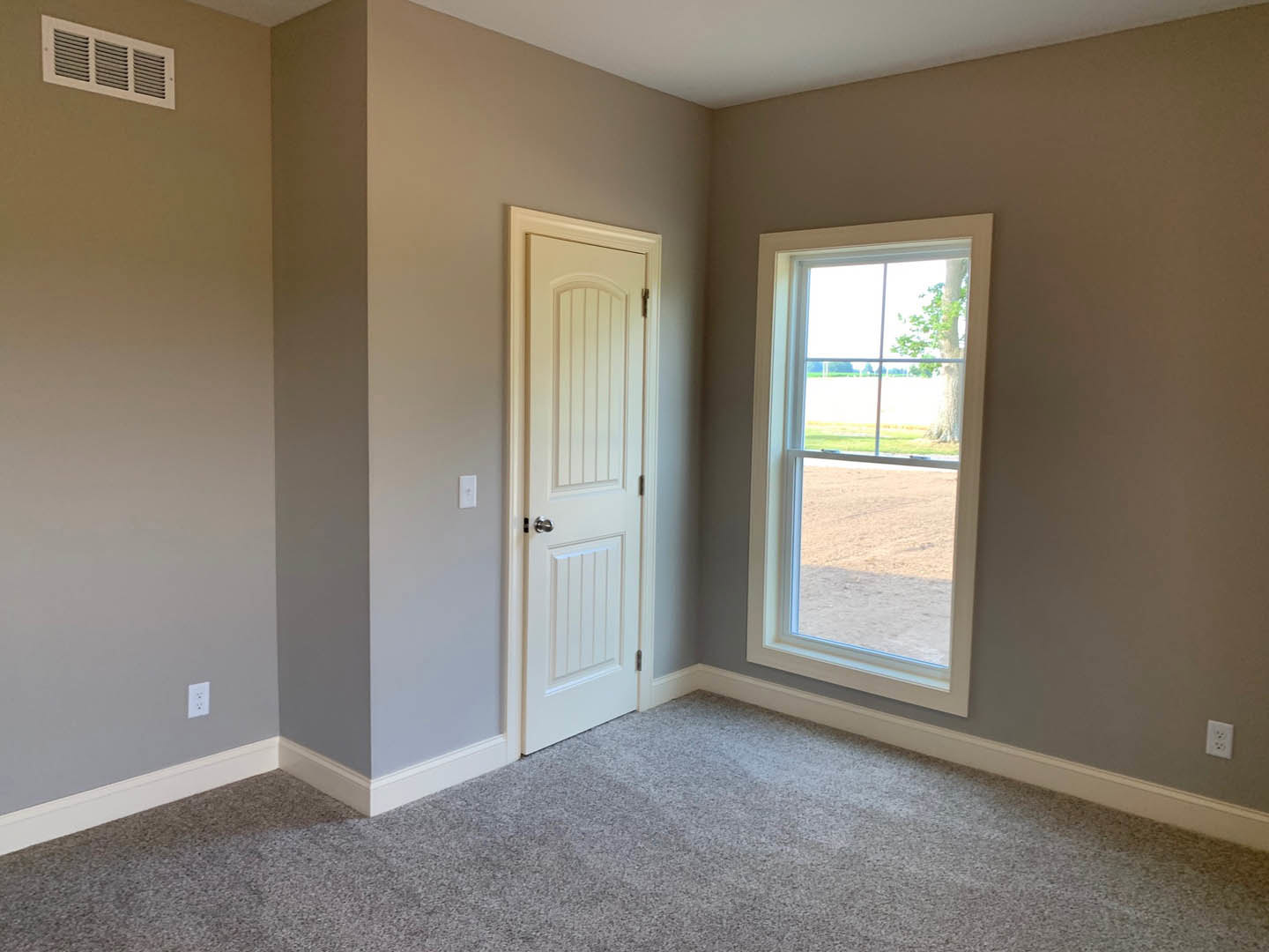 White door and window in a carpeted room, tree visible outside, wall vent and plaster walls