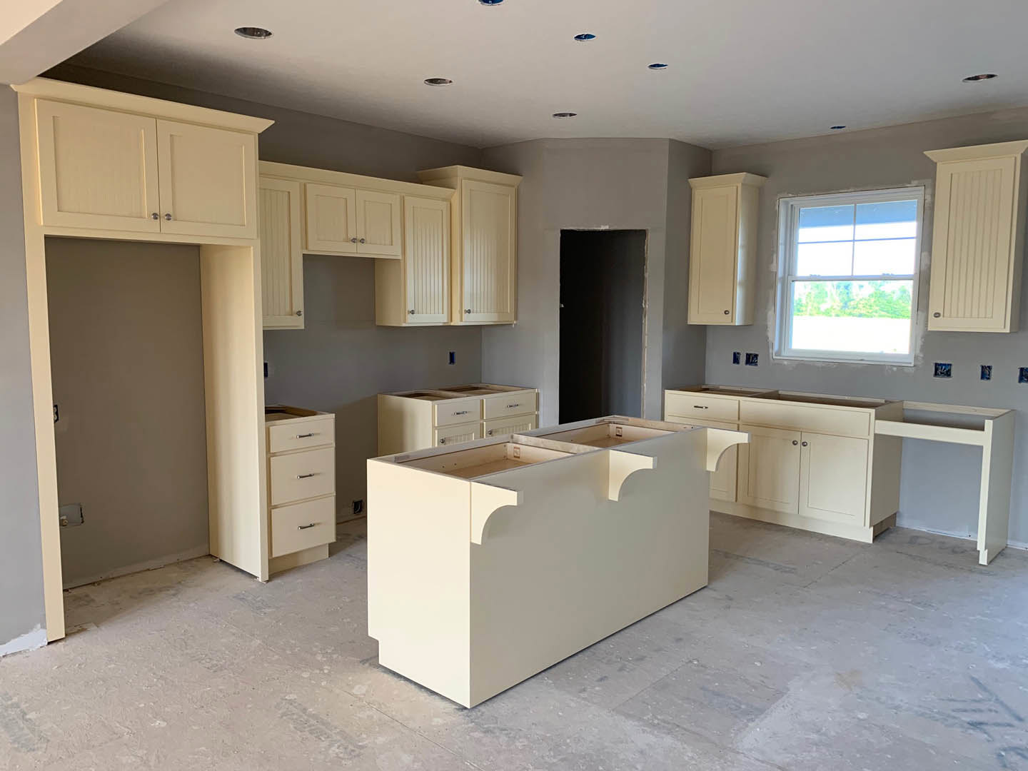 Modern kitchen featuring white cabinetry and drawers, sleek white countertop with open shelving, window framed in white, close-up of a drawer, vertical-lined white door, and dark