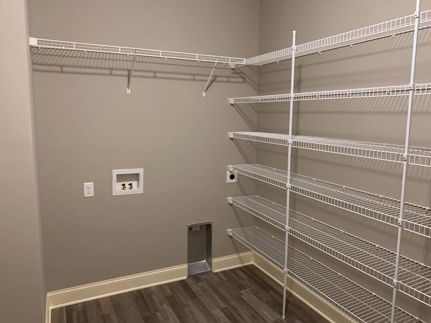 Empty walk-in closet with white built-in shelves, wood flooring, and a silver metal object placed on the floor.