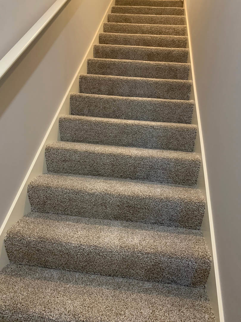Carpeted staircase with wooden handrail and white painted walls, shown in close-up view