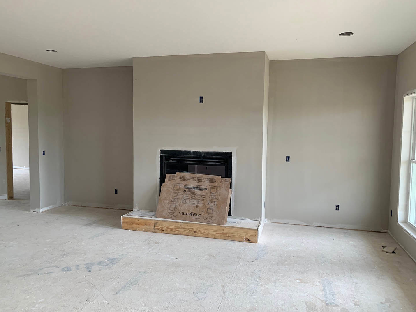 Living room with white plaster walls, wood plank flooring, central stone fireplace, and large window letting in natural light
