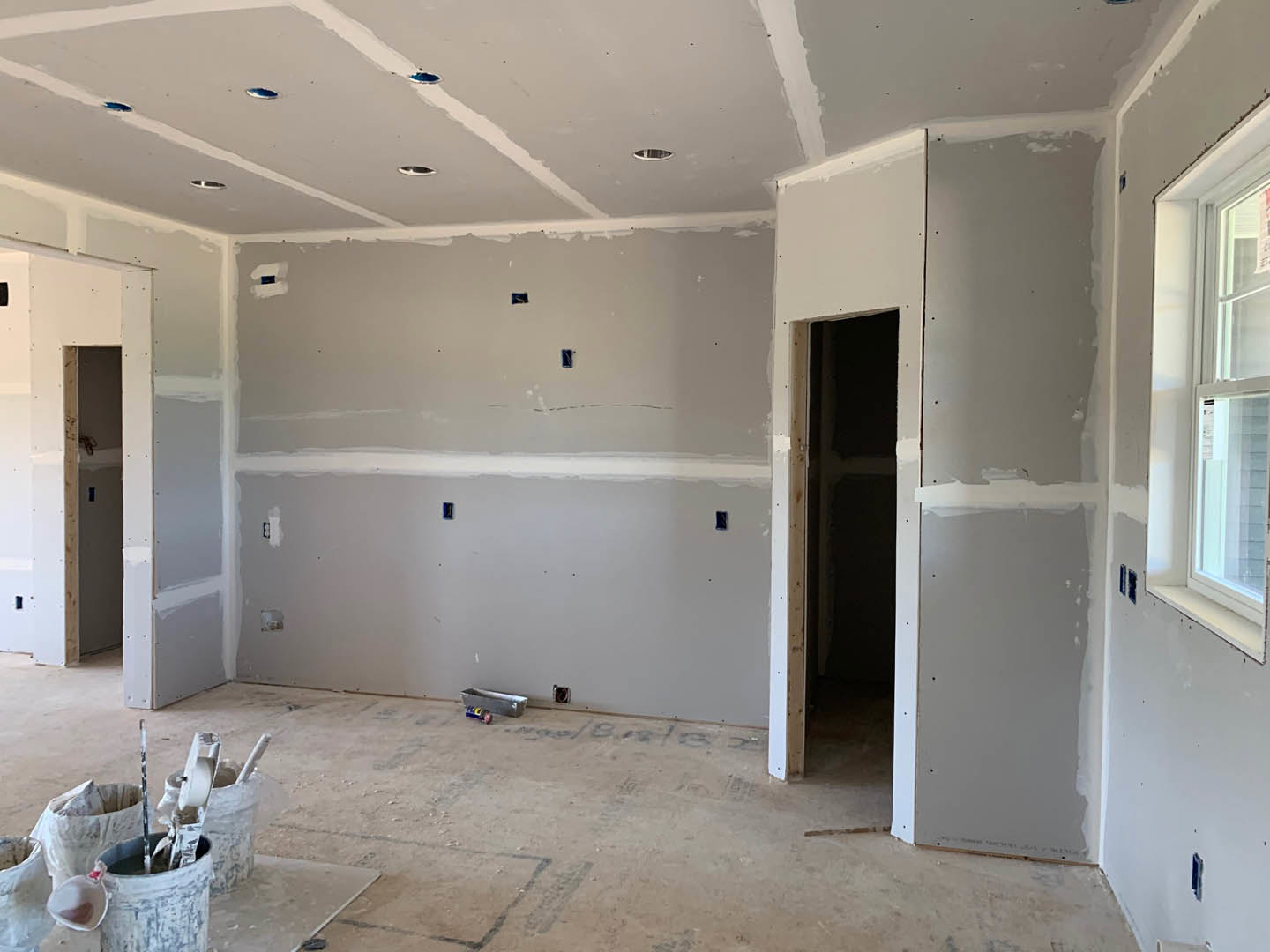 White-walled room with tile flooring, paint buckets, and painting tools scattered near a window and door.