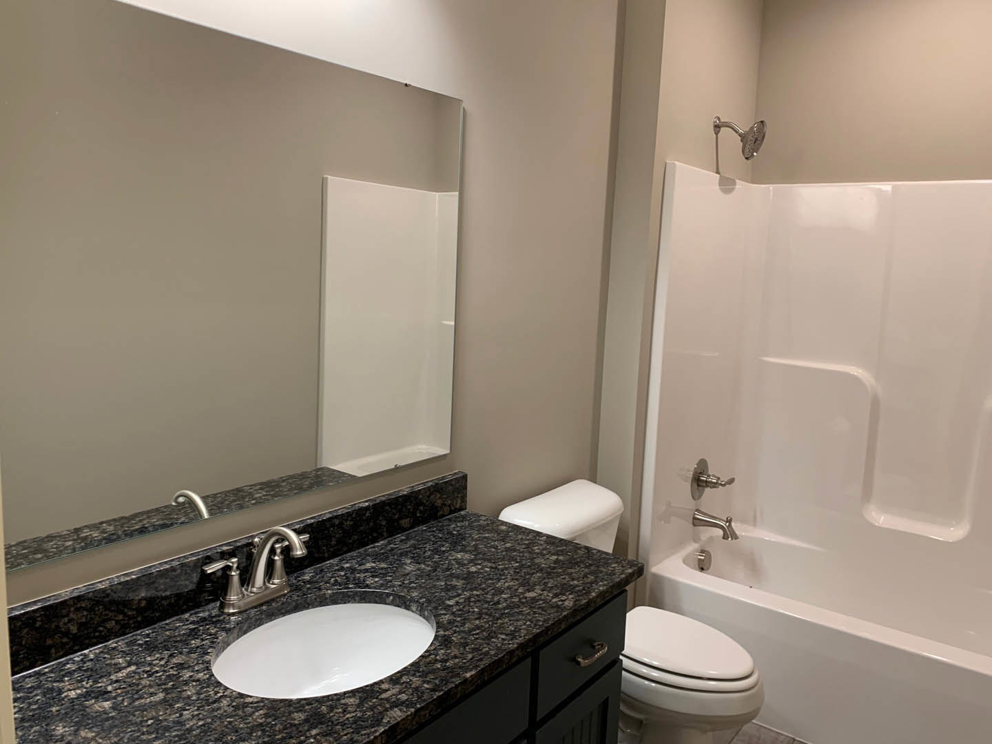White oval sink set in marbled countertop, chrome faucet, glass-enclosed shower with tile walls, white painted walls, metal-framed mirror