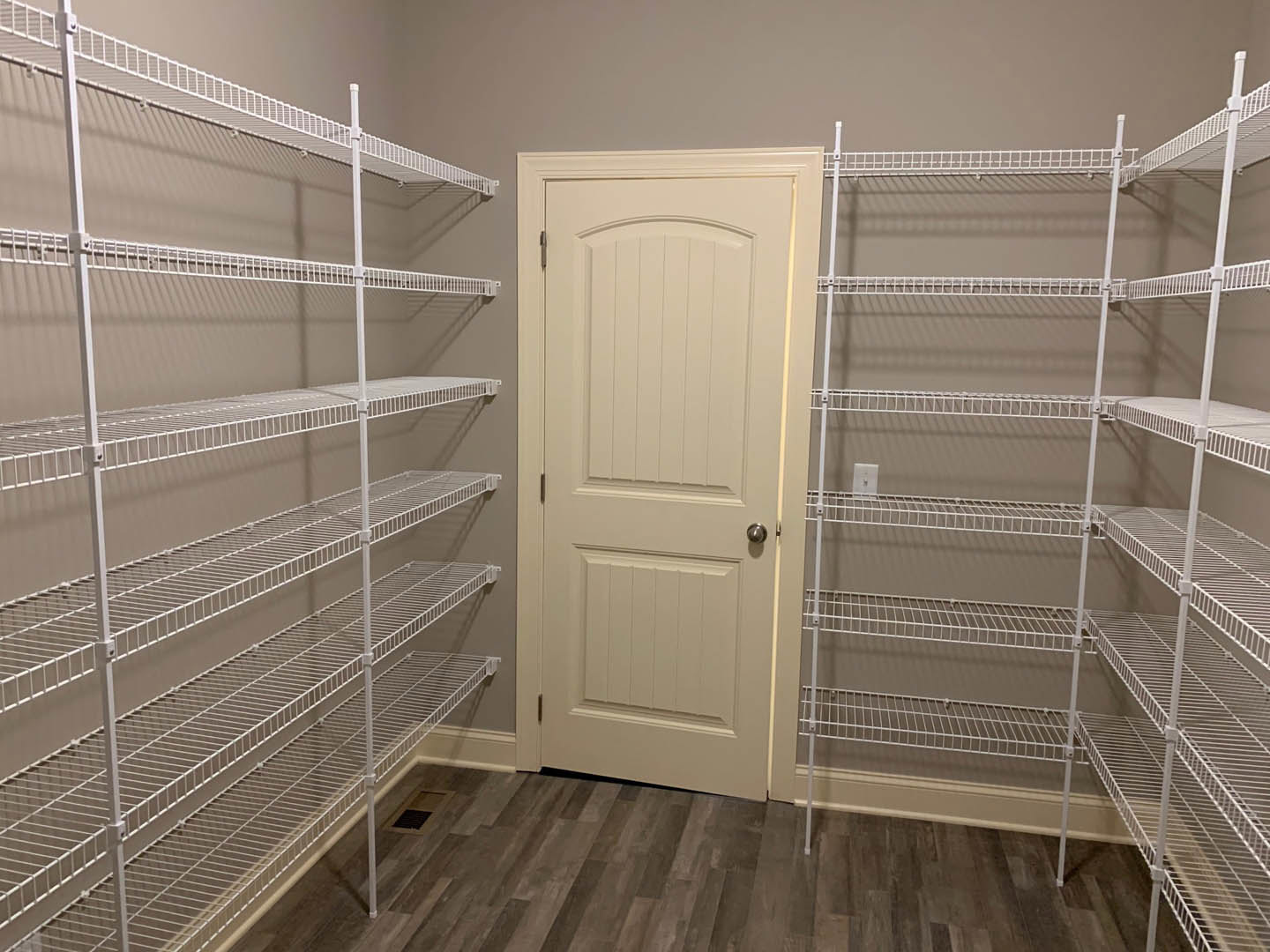 White built-in shelves and cabinet beside a closed white door with silver knob, set on light wood flooring in a neutral-walled room.