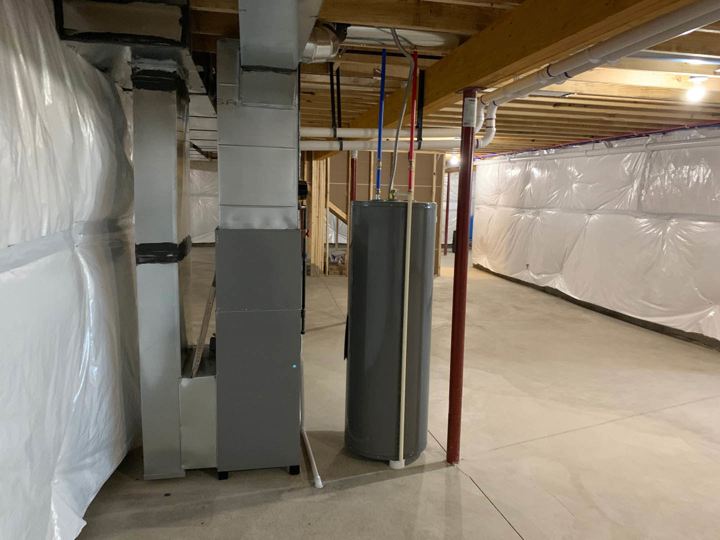 Utility room with exposed steel and aluminum pipes along a wall, grey electrical box, plastic sheeting, and concrete floor