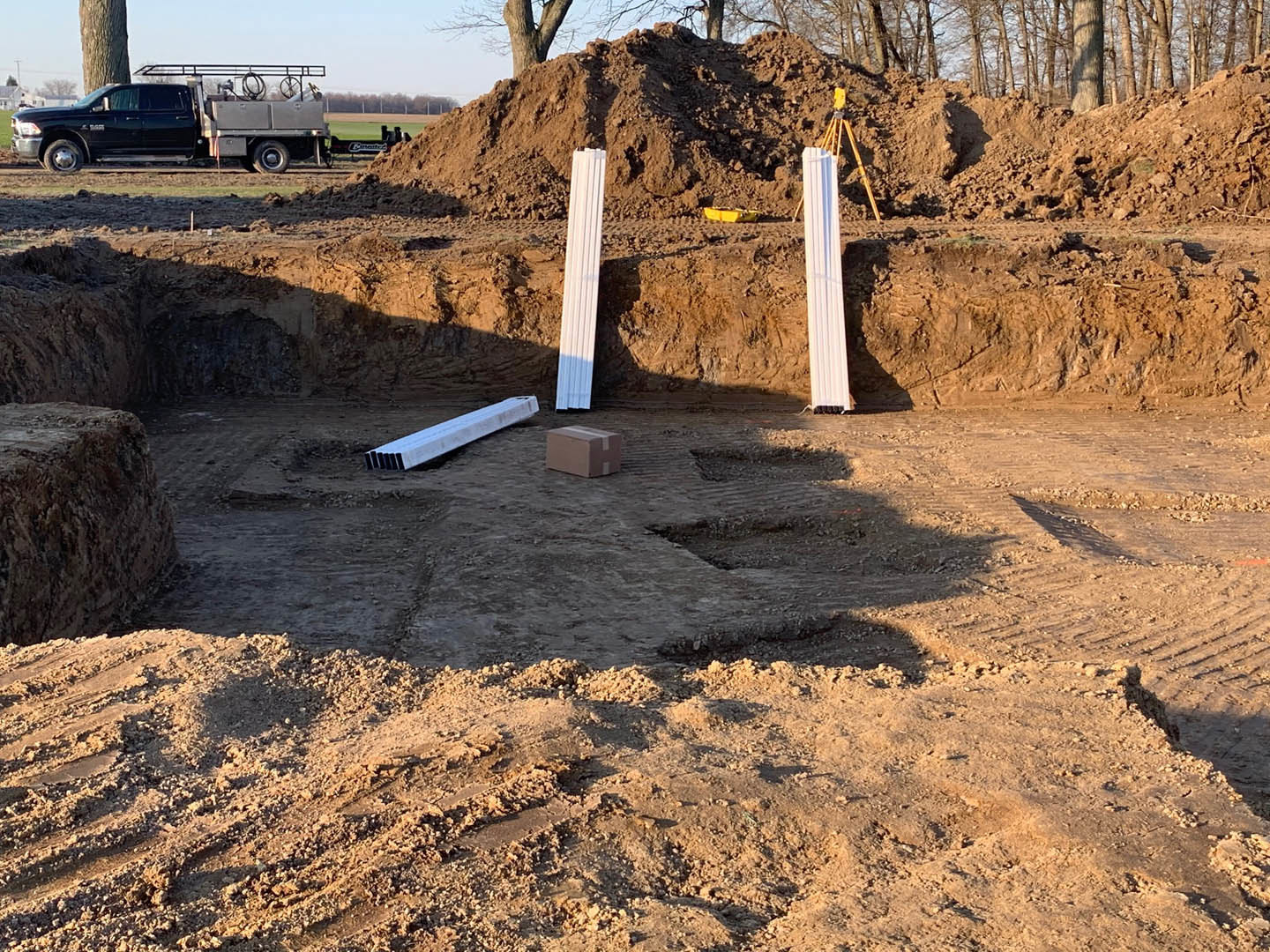 White metal beams stacked on a dirt pile in a construction site, black truck with ladder parked nearby, white rectangular object resting on wooden surface, close-up of white post