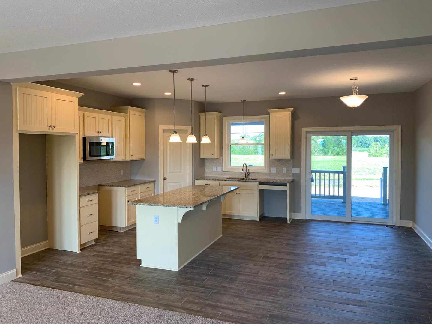 Kitchen and dining area featuring a granite-topped island, white cabinetry with metal handles, built-in microwave, wood flooring, and a sliding glass door overlooking a grassy