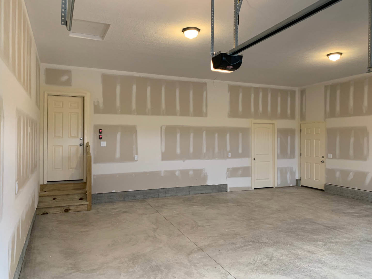 White-walled room with white doors, concrete flooring, silver and black door handles, plaster ceiling, and simple molding
