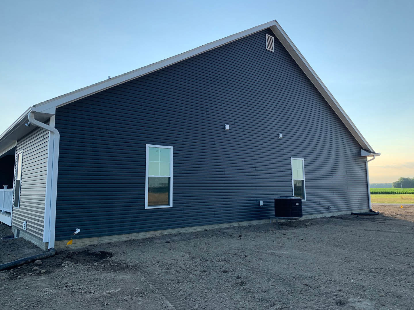 Blue metal roof atop a white-sided cottage, square windows, dirt yard in foreground, clear sky overhead