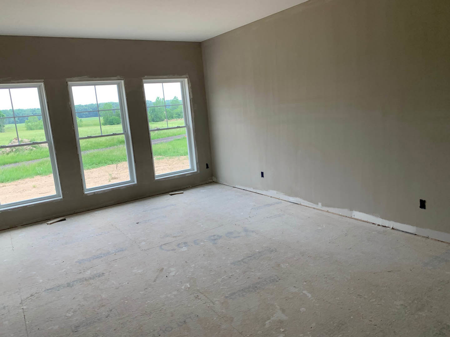 Bright room with large windows, white plaster walls, light wood flooring, and views of a grassy field and trees outside