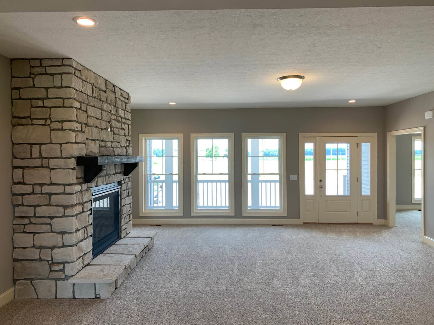 Living room with tile fireplace, white door with glass panes, large window with white railing, light-colored flooring, and neutral walls