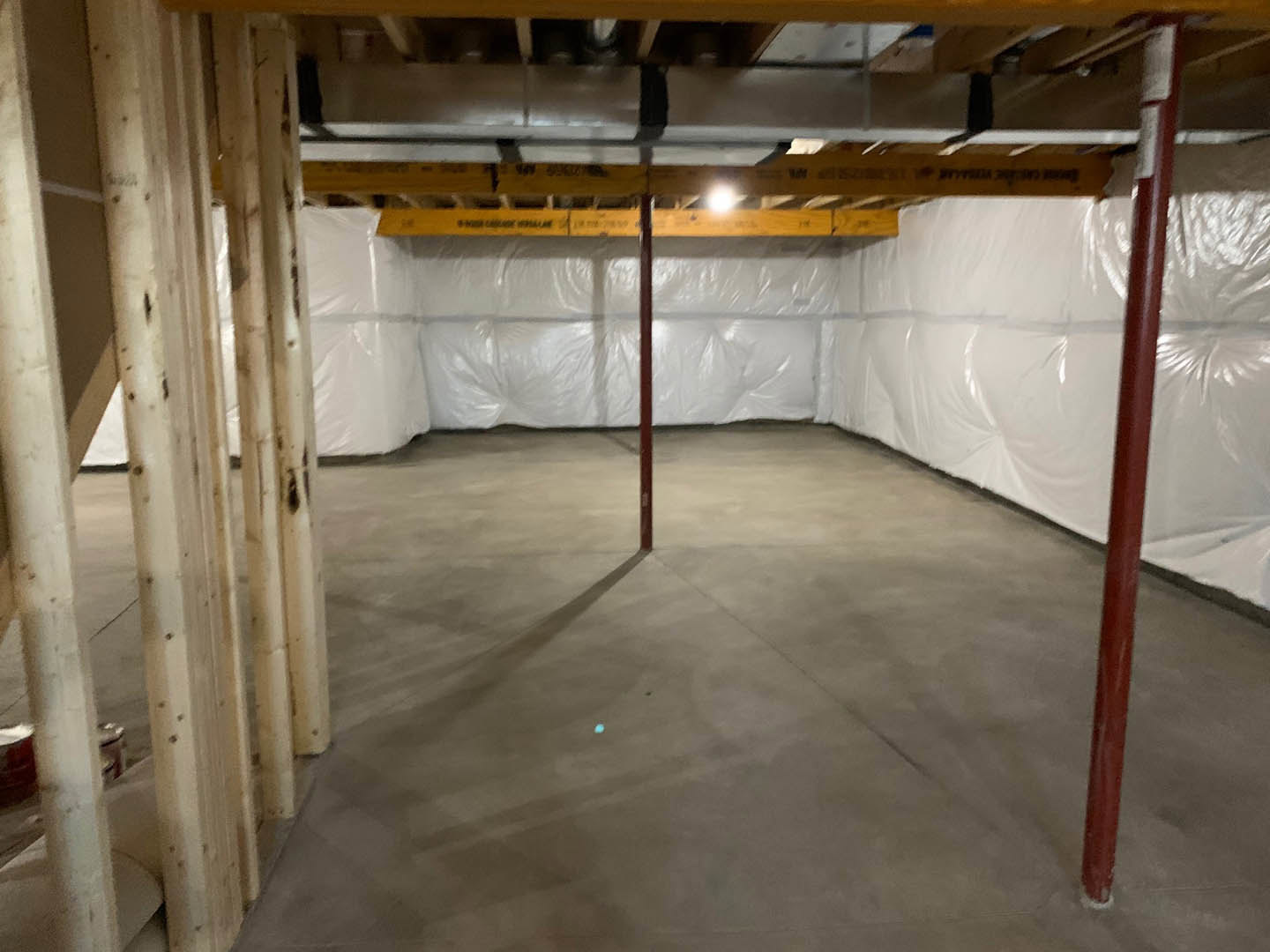 White plaster wall, exposed red metal support pole, concrete floor, unfinished ceiling with visible insulation in basement room