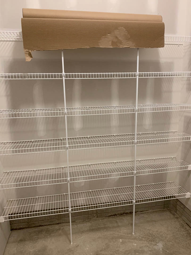 White wire shelving mounted on an interior wall, holding a brown cardboard sign with printed text.