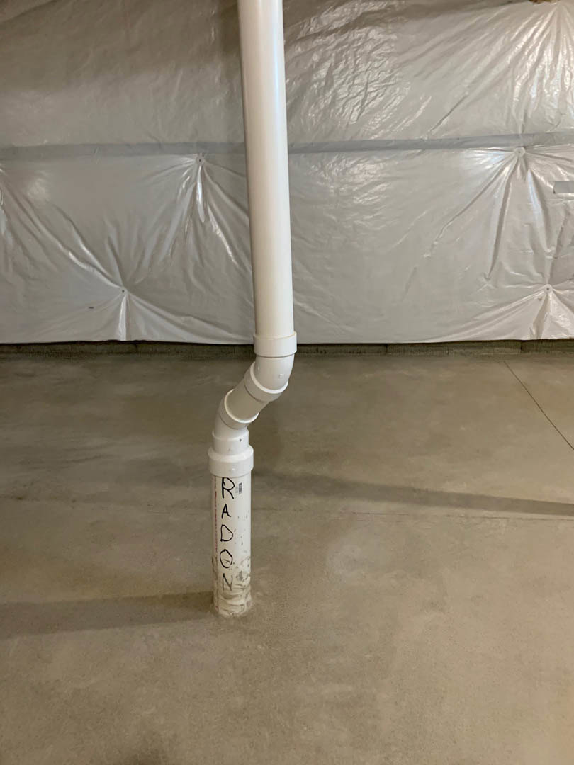 White plastic pipe with black writing and black handle resting on light-colored floor in a room with white walls.