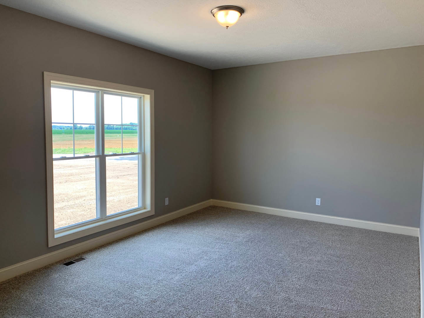 Carpeted room with white walls, large window overlooking grassy field, white ceiling with recessed light fixture, simple baseboard molding