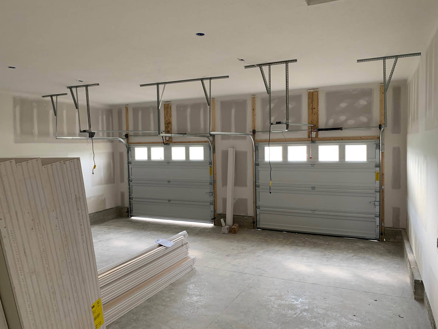 Spacious garage with multiple white paneled doors featuring window inserts, smooth plaster walls, white ceiling with recessed lighting, light-colored concrete floor, exposed brick
