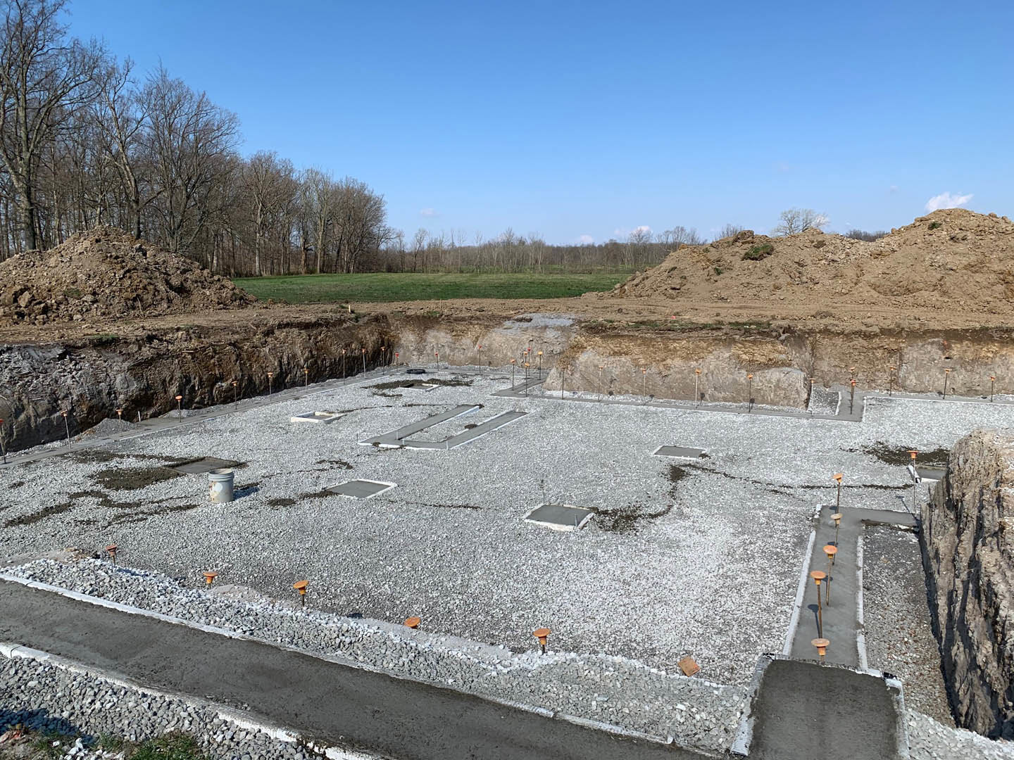 Dirt hill with scattered rocks and gravel, surrounded by trees under a partly cloudy blue sky at a residential construction site