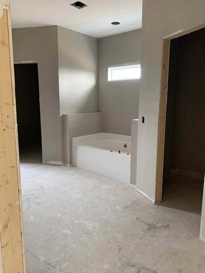 Modern bathroom featuring a freestanding white tub beneath a large window, light gray tile flooring, plaster walls, and minimalistic fixtures.