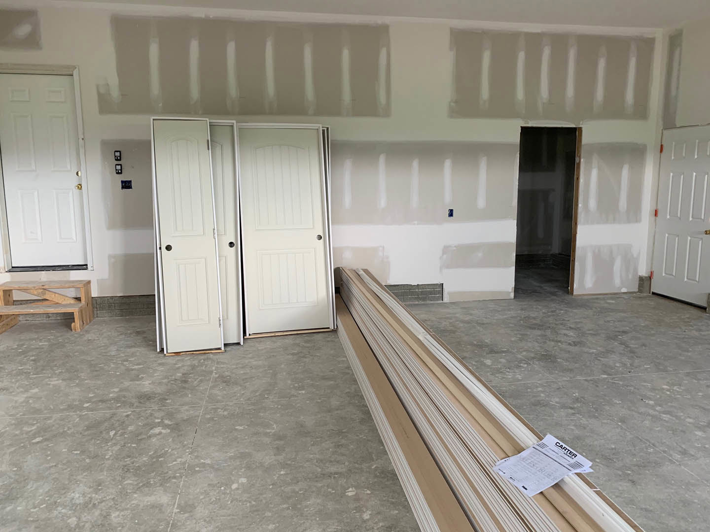 White-walled room with white trim, light wood flooring, white doors with gold handles, and a wooden bench.