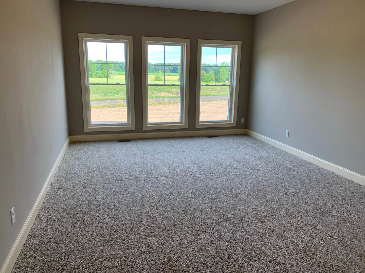 Carpeted room with a row of large windows overlooking grassy field and trees