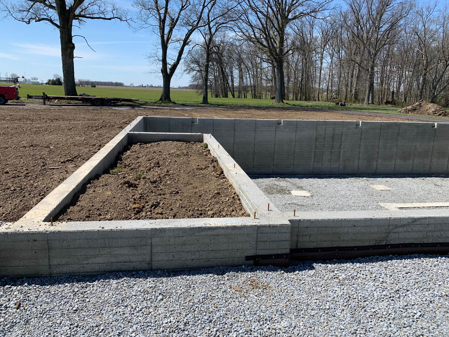 Concrete foundation filled with dirt, surrounded by trees and open field under a clear sky