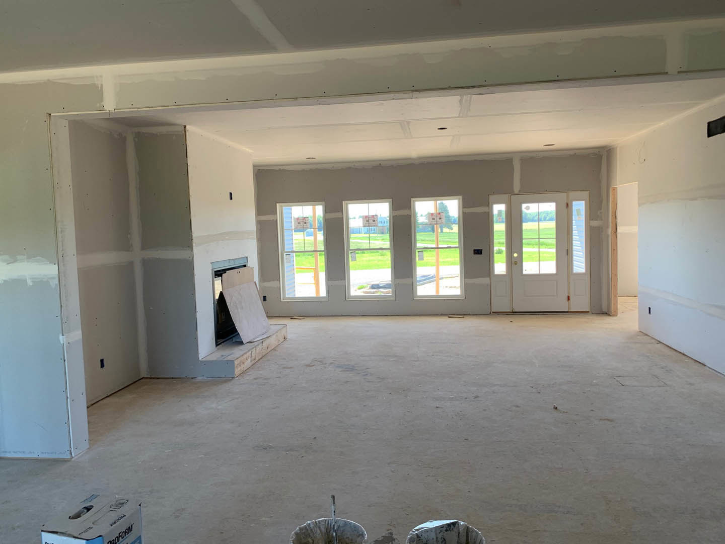 Living room with stone fireplace, large windows, white plaster walls, wood flooring, and glass-paneled door