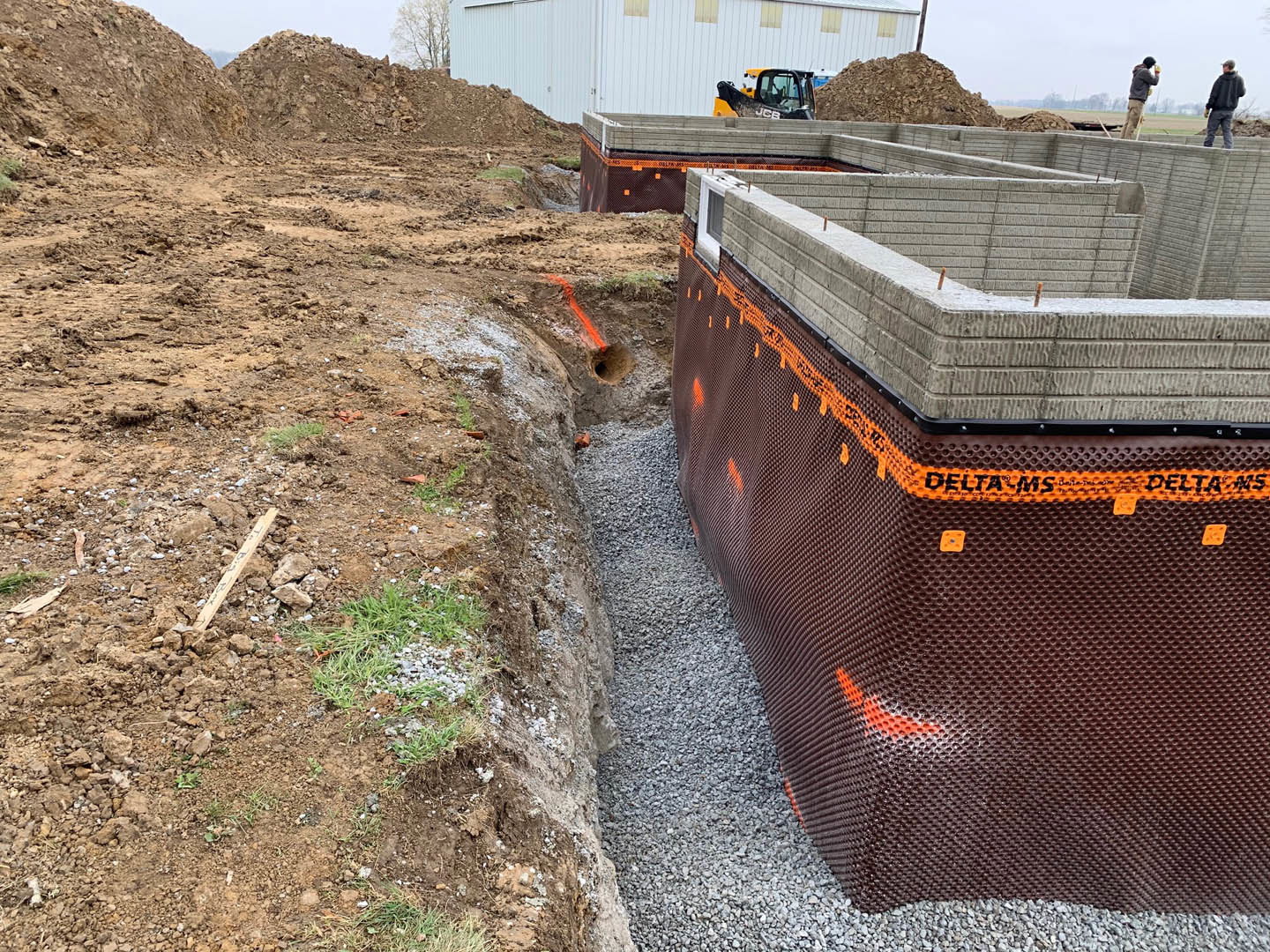 Framed custom home under construction with exposed wooden beams, large metal pipe on dirt ground, partially finished roof, and open sky in background