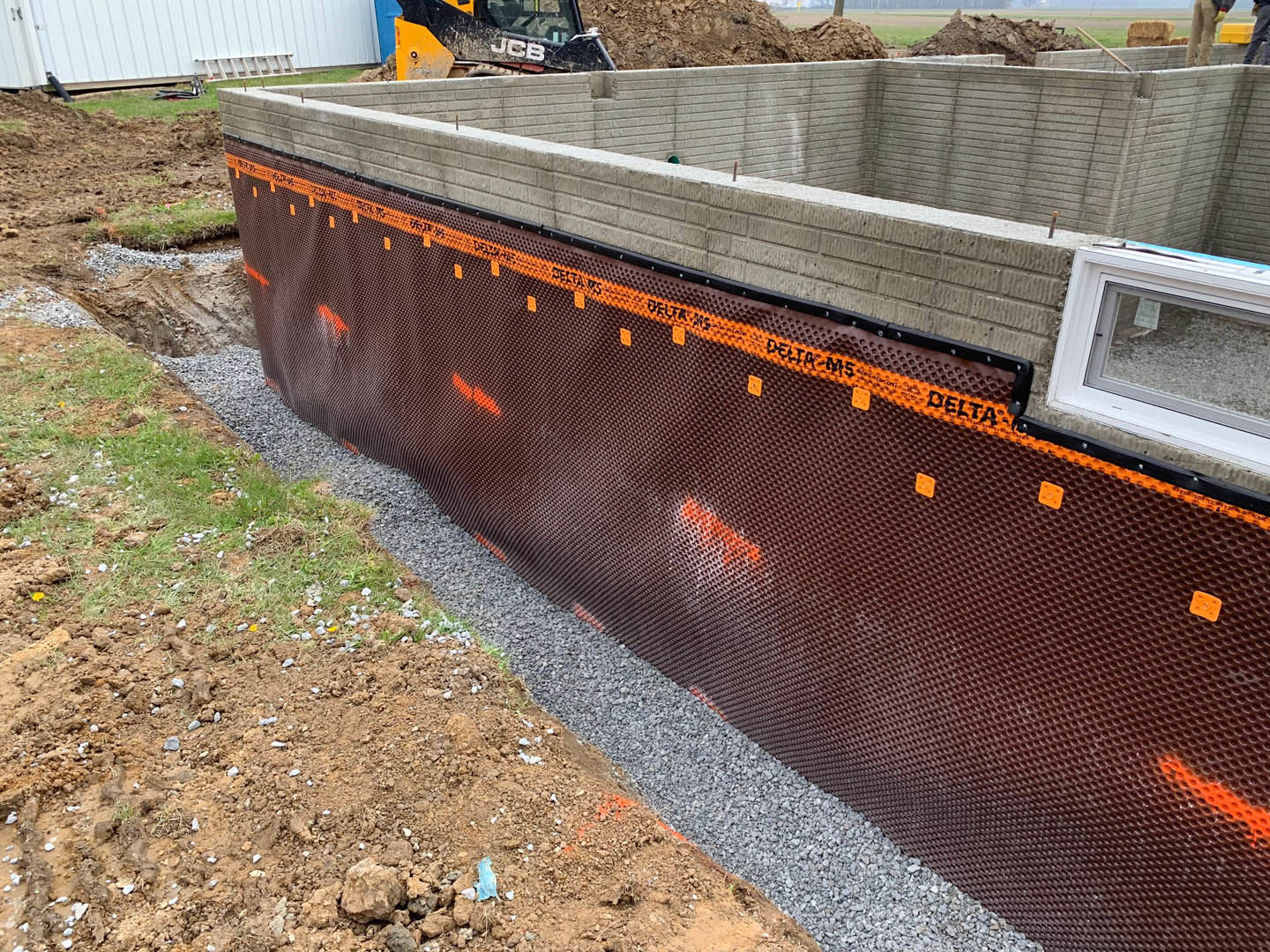 Gravel construction site with white exterior wall, metal fence, ladder, and construction vehicle