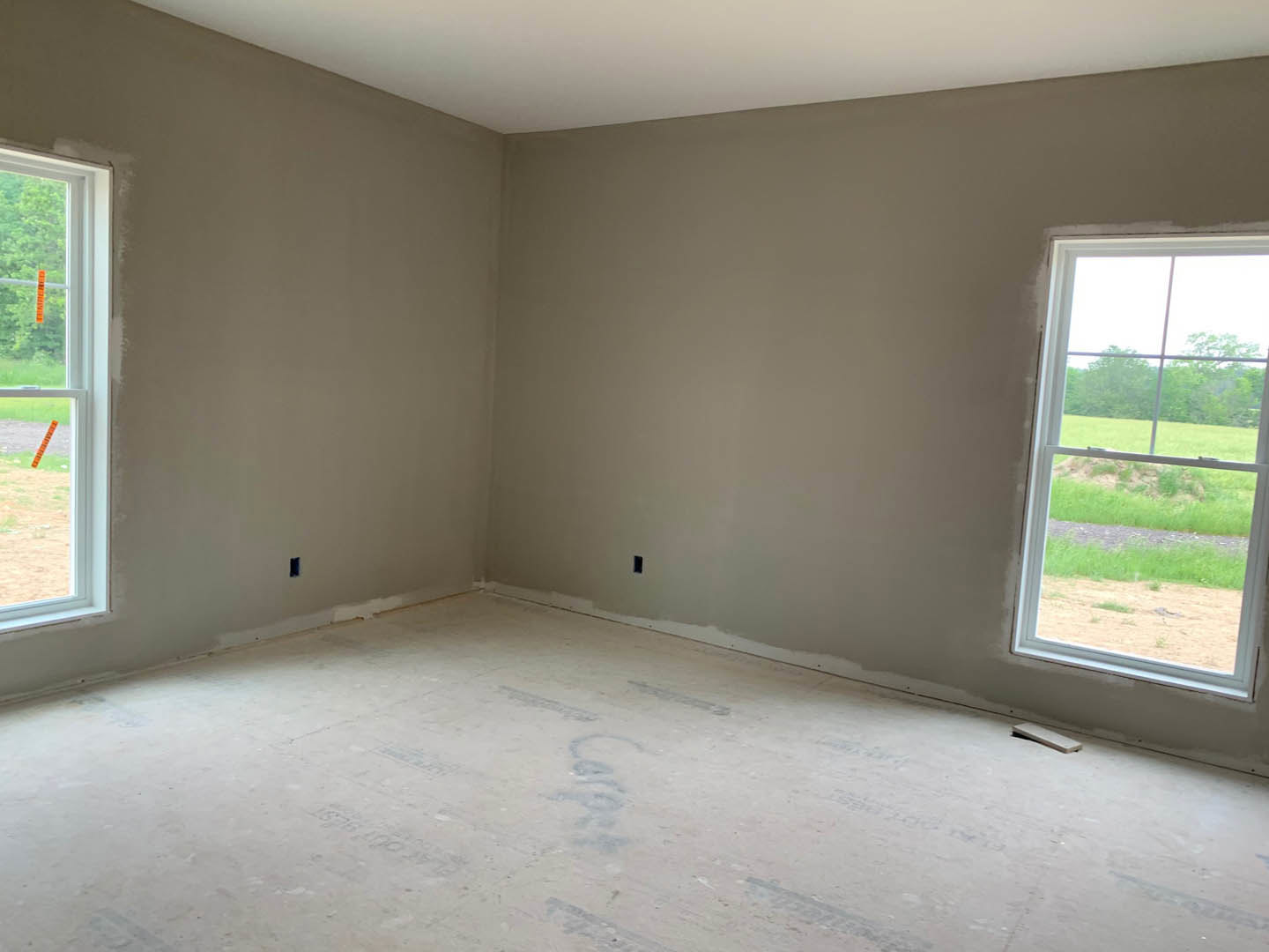 Modern room with two large windows, concrete flooring, white plaster walls, and views of a green grassy field outside