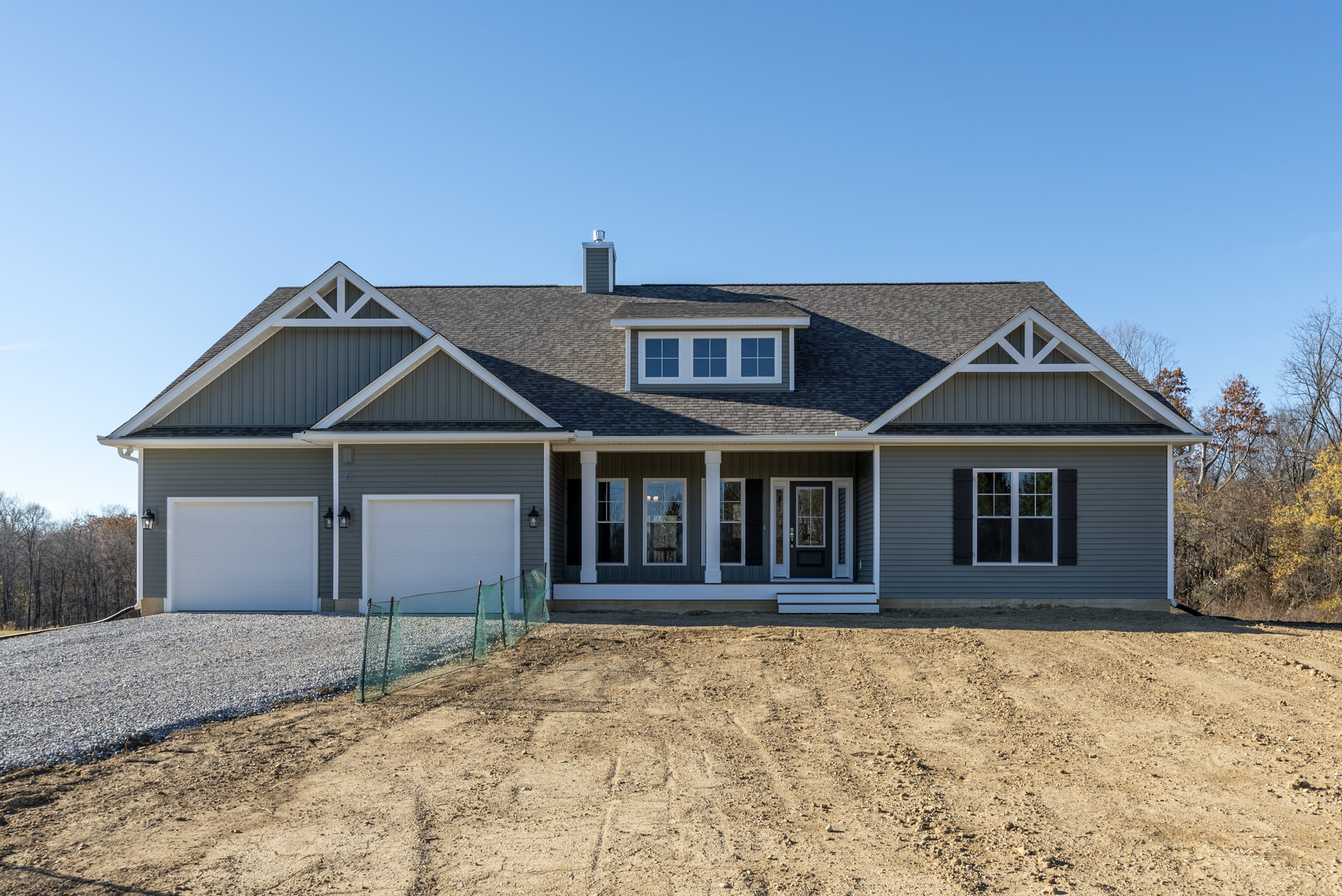 Two-story home with light siding, white-trimmed windows, attached garage, paved driveway, and fenced yard with green mesh fencing
