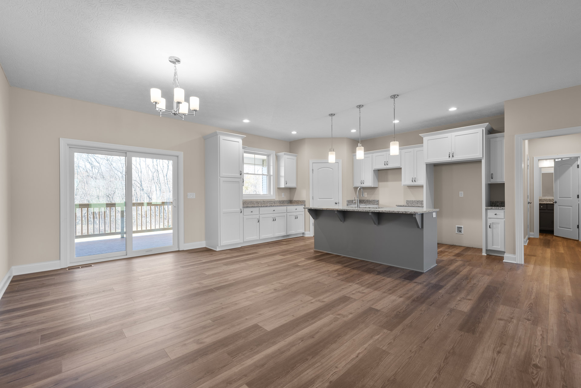 Kitchen with hardwood floor, white cabinets, bar seating, sliding glass door opening to deck and trees, white framed window, white door with silver knobs, stone countertop with