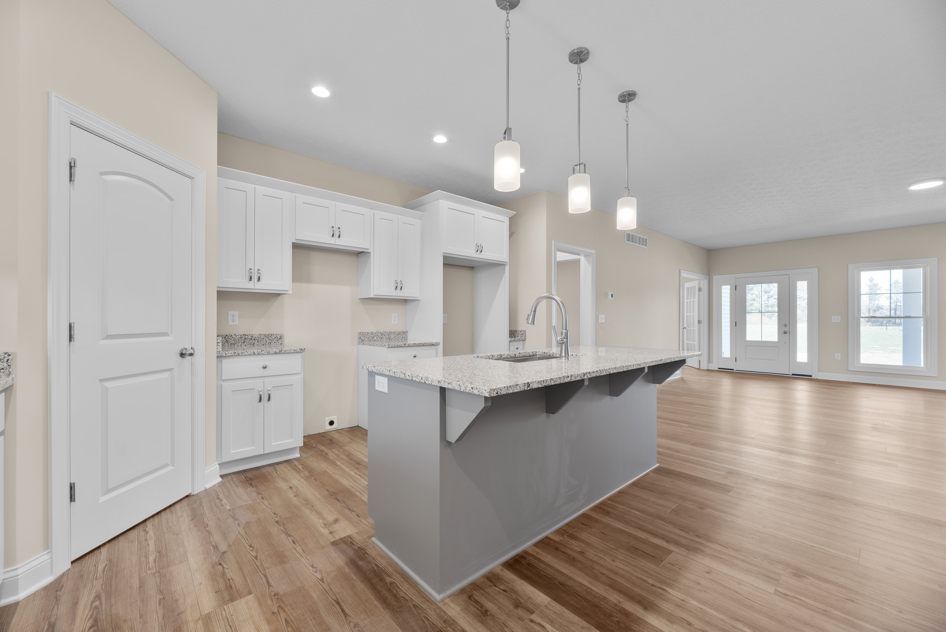Spacious kitchen featuring a large island with built-in sink, wood flooring, white cabinetry, and a window overlooking a field; white doors with glass panes and silver hardware