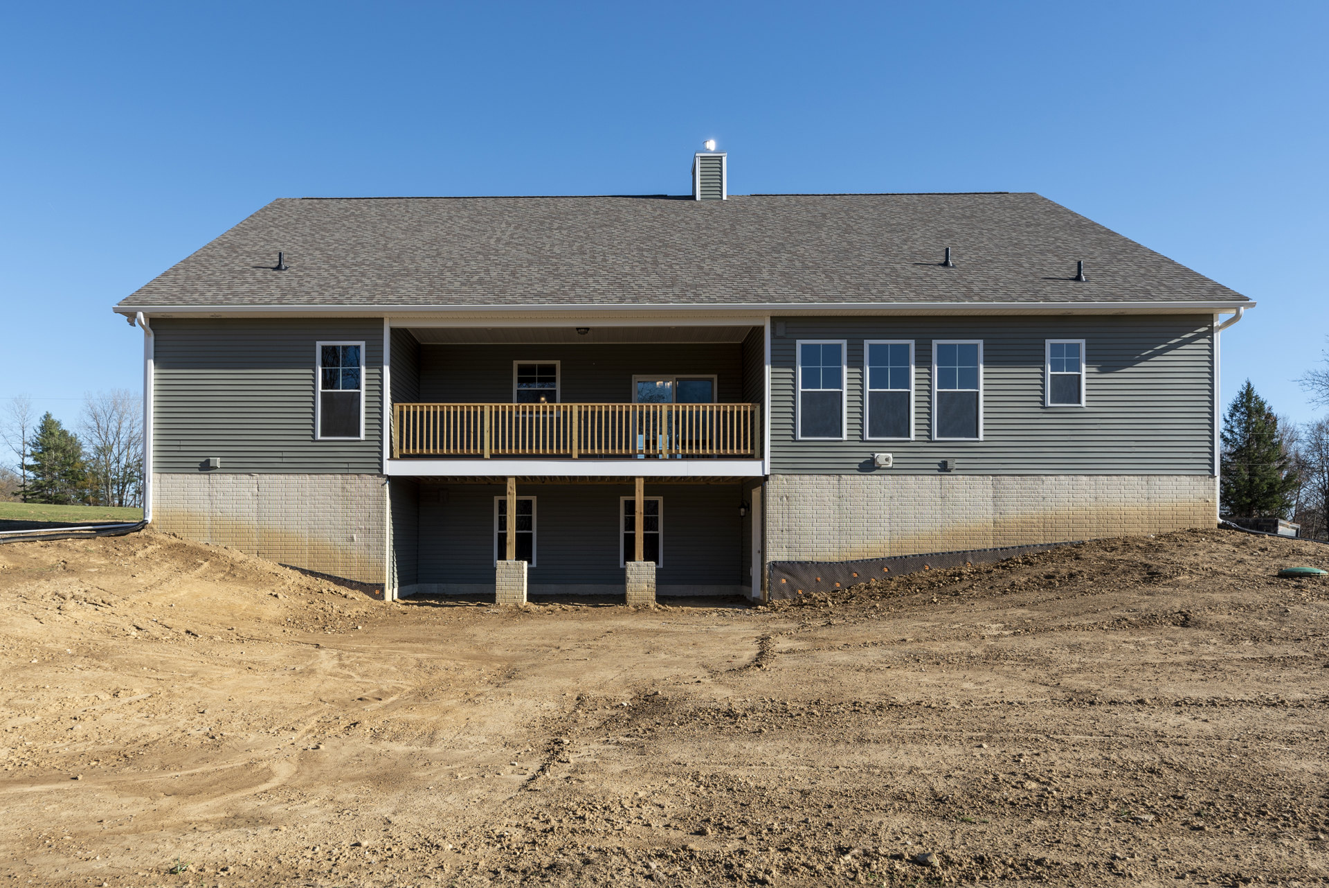 Two-story house with white-framed windows, wooden porch railing, elevated balcony, and dirt hill in front yard