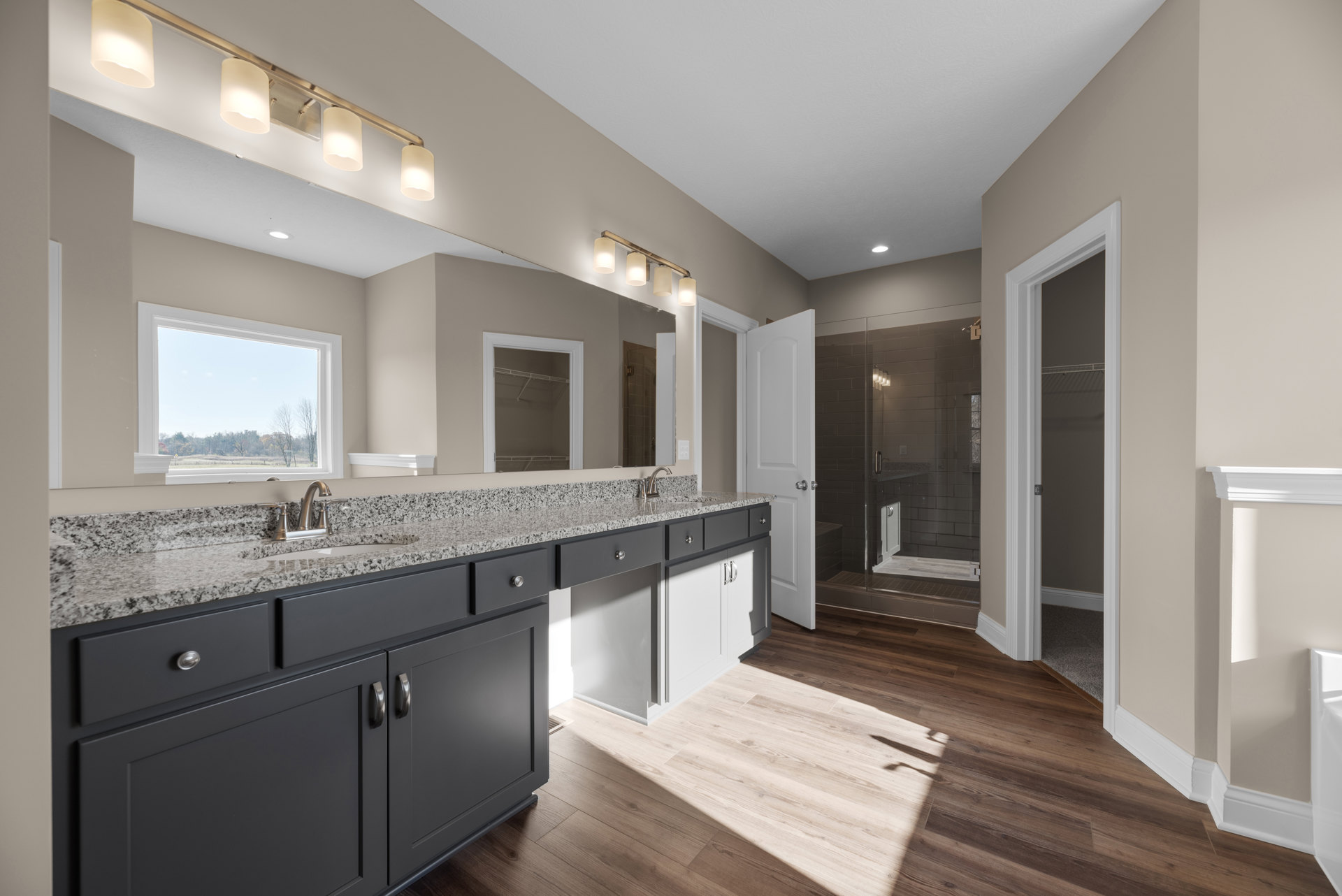 Bathroom with granite countertop, double sinks, large wall mirror, tile flooring, window overlooking trees, white cabinetry, and modern light fixtures